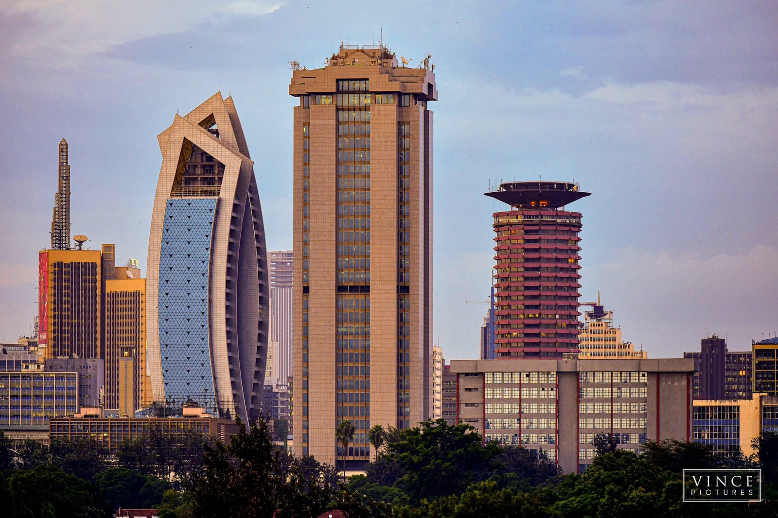 The Nairobi skyline at golden hour with the flat-topped CBK Pension Towers at centre, the glass Britam Tower to the left and the cylindrical KICC to the right