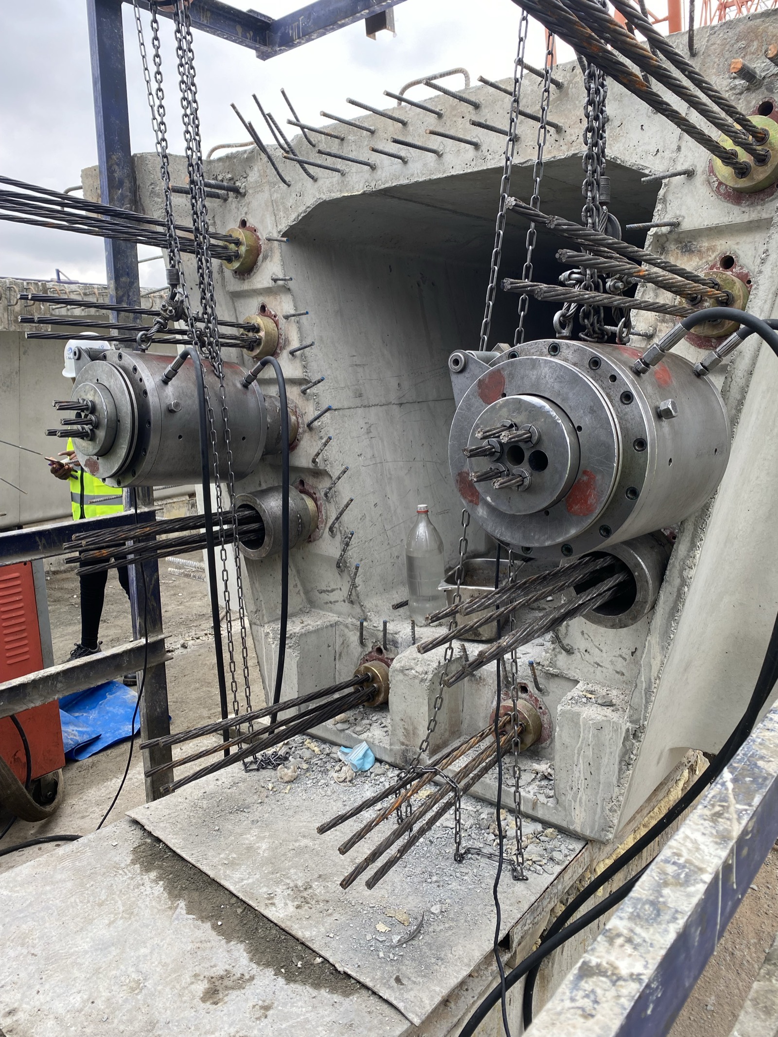 Two multi-strand stressing jacks suspended on chains at a concrete deck anchorage on the Nairobi Expressway, seven-wire strand fanning from the anchor heads