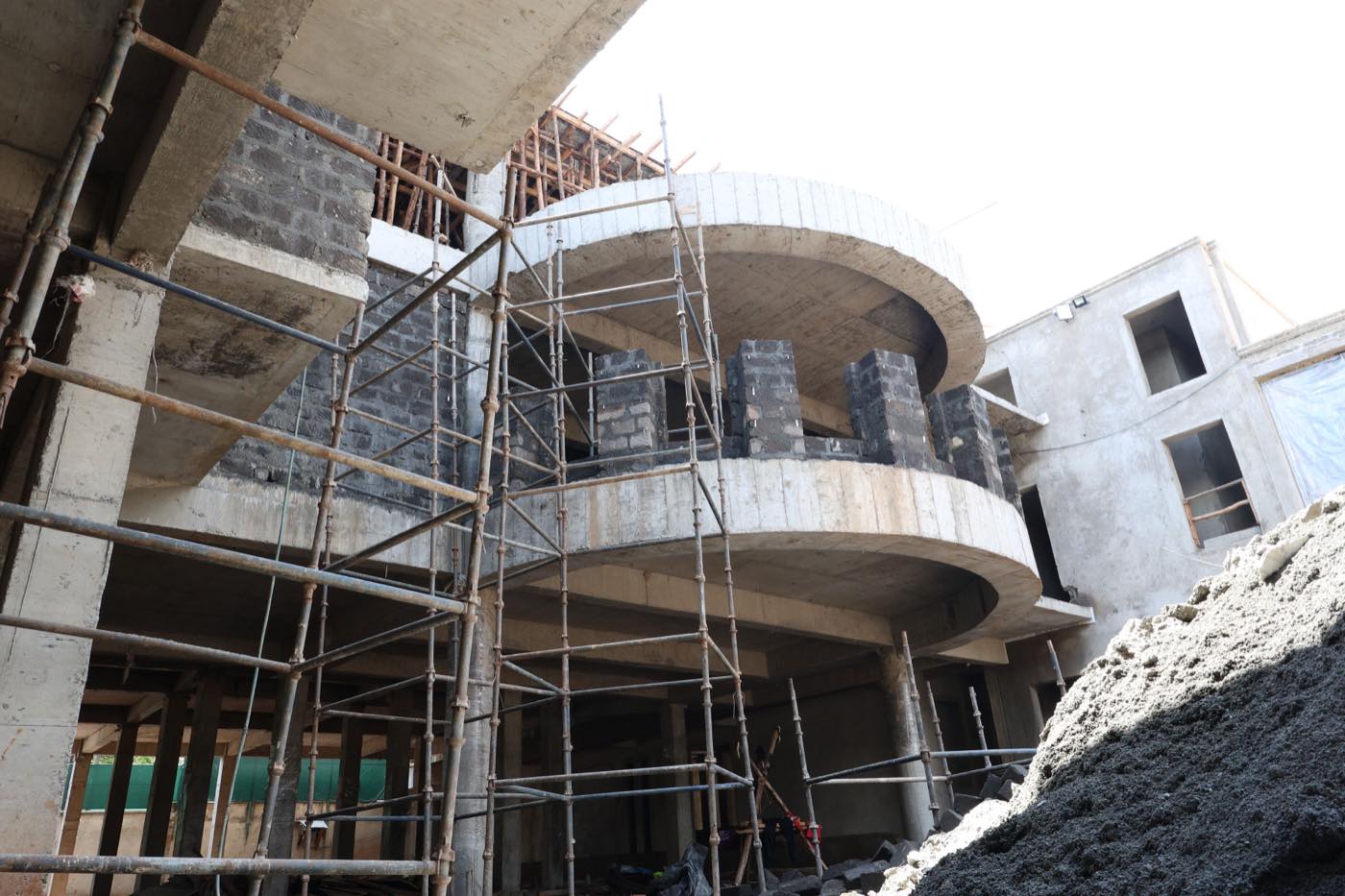 Curved reinforced-concrete balcony wings of the Kitisuru hotel rising behind full-height scaffolding