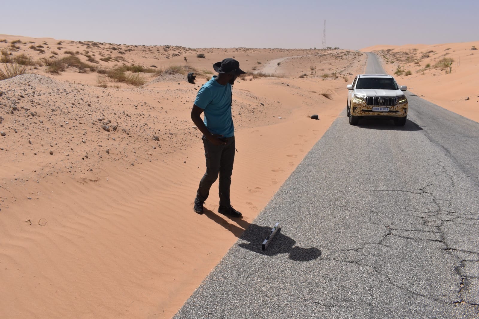 A straight-edge camber check where dune sand overruns the carriageway edge on the Nouadhibou to Zouerat road, Mauritania