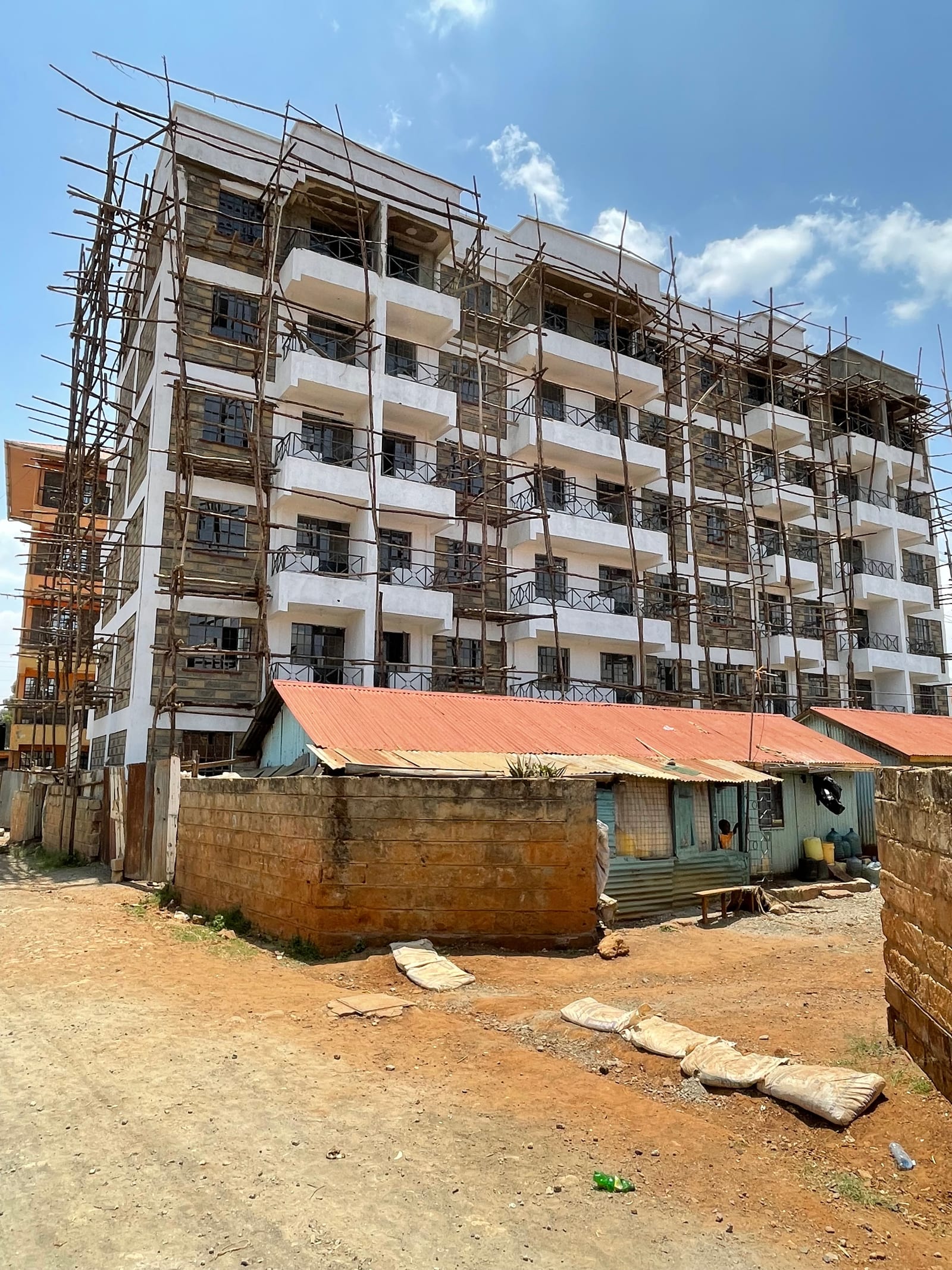 The ACK Trinity Muthua residential apartment block in Uthiru, Nairobi, rendered white above a terracotta base and wrapped in timber scaffolding