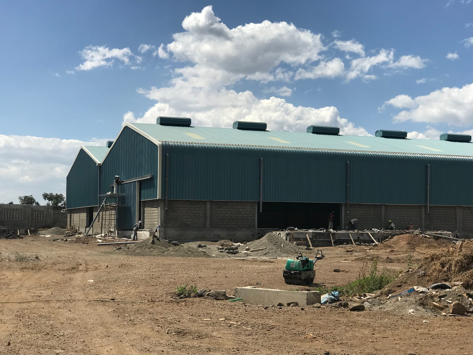 The green metal-clad exterior of a VisionOne warehouse under construction in Nakuru, a curved roof with ridge vents over a masonry plinth